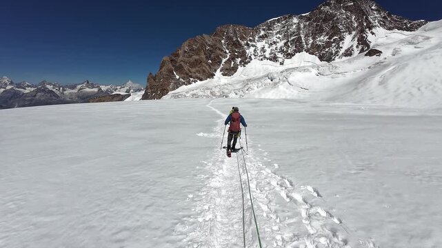 POV mountaineering in rope team with mountaineers descending on glacier Grenzgletscher and mountain panorama with summit Dufourspitze in Pennine Alps, Switzerland