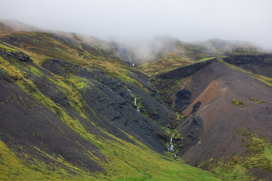 Icelandic mountains with waterfalls and green moss under fog