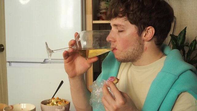 Young man drinks wine and prepares to eat vegetables