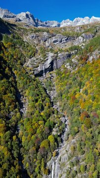 Aerial view of the Val di Mello waterfall cascading down rocky cliffs surrounded by colorful autumn forest and mountain peaks in Val Masino, Lombardia, Italy.