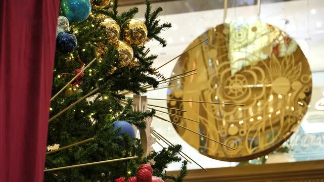 A decorated Christmas tree against the backdrop of a swinging clock pendulum.