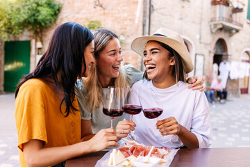 Female friends laughing together with red wine outdoors. Young women enjoying relaxed lifestyle moment in European city. Lifestyle and friendship concept. © Xavier Lorenzo
