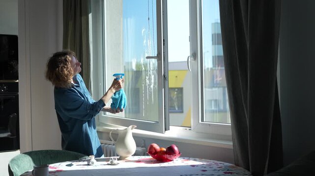 Woman washes windows in her home on a sunny day