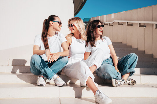 Three young beautiful smiling hipster female in trendy summer white t-shirt  and jeans clothes. Sexy carefree women posing in street. Positive models having fun, going crazy. In sunny day