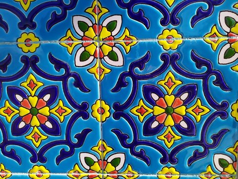 Colorful decorative tile with floral and geometric motifs in blue yellow and red forming a vibrant traditional pattern that reflects cultural design symmetry and artistic craftsmanship.