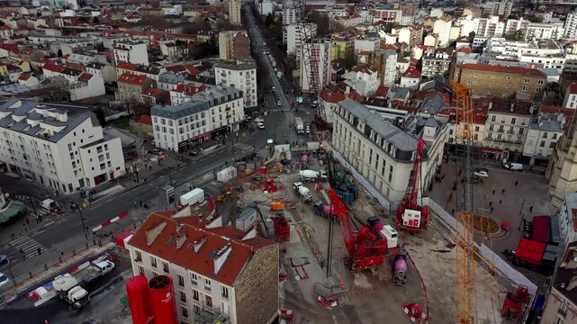 Large urban construction site with cranes and cement mixers surrounded by city traffic in Paris, France. Aerial tilt-down forward