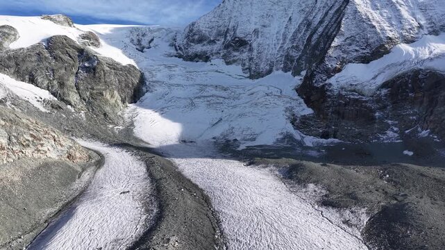 Aerial flyover over the glacial tongue of Glacier de Cheilon on a sunny summer day in the Swiss Alps with a view towards the mountain peaks of Arolla such as Mont Blanc de Cheilon