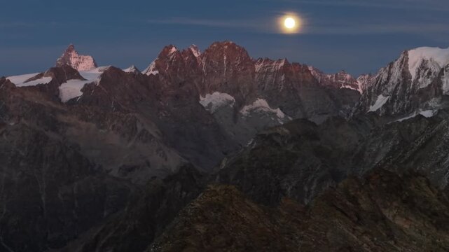 Aerial view of the Matterhorn and other peaks in the Swiss Alps during a summer evening with a full moon shining above the horizon