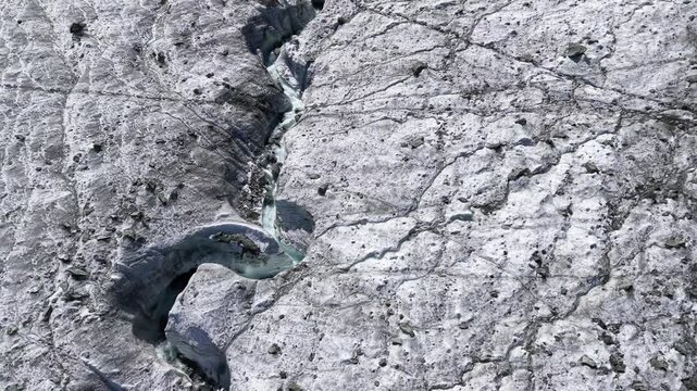 Aerial flyover over the ice of Glacier de Cheilon with a pan up view from the crevasses and moraines to the mountain peaks of the Swiss Alps