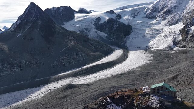 Aerial view of a mountain hut alongside Glacier de Cheilon as the morning sun shines over the mountain peaks of Swiss Alps in the Arolla region