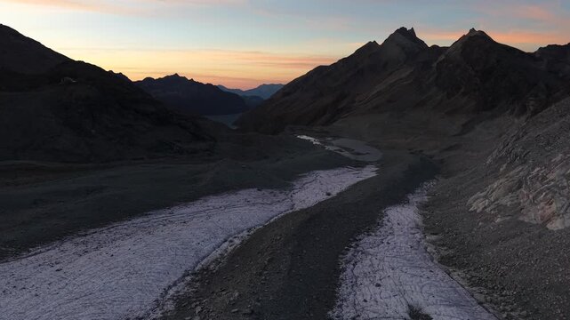 Aerial flyover towards the glacial lake of Glacier de Cheilon a sunset in the Swiss Alps with a view of the ice, moraines and glacial tongue with a colorful sky glow