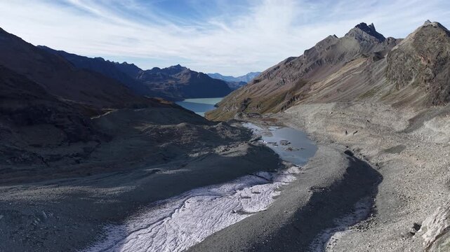 Aerial flyover over the glacial tongue of Glacier de Cheilon on a sunny summer day in the Swiss Alps with a pan down view from the blue glacial lake towards the icy crevasses and moraines.