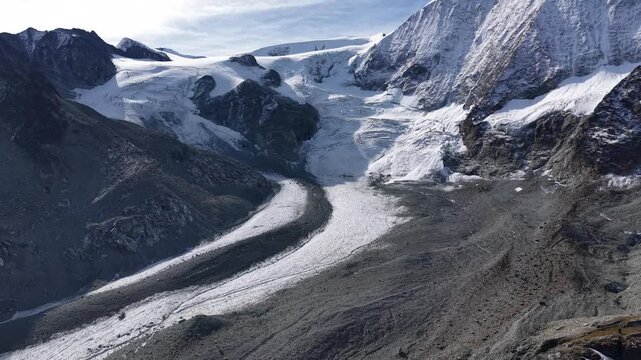 Aerial flyover around mountain hut alongside Glacier de Cheilon as the morning sun shines over the mountain peaks of Swiss Alps in the Arolla region