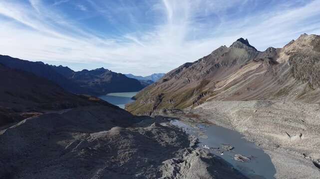 Aerial flyover across the glacial tongue of Glacier de Cheilon on a sunny summer day in the Swiss Alps with a pan down view towards the icy blue glacial lake.