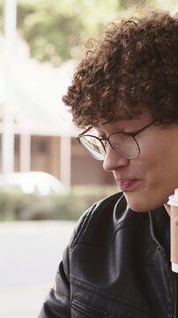 Vertical video: Raising cup, man in leather jacket and glasses sipping and speaking to left at cafe