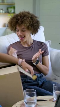 Vertical video: Hands cutting tape on box, woman brown tee at home reaching pulling wrap to inspect