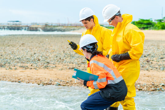 Environmental engineers and hazardous material inspectors analyzing water samples at industrial site, scientists in protective suit performing wastewater pollution monitoring and contamination testing