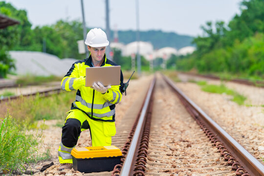 Railway engineer inspecting railroad track with laptop and radio communication device during railway maintenance operation, industrial transportation infrastructure worker checking rail system