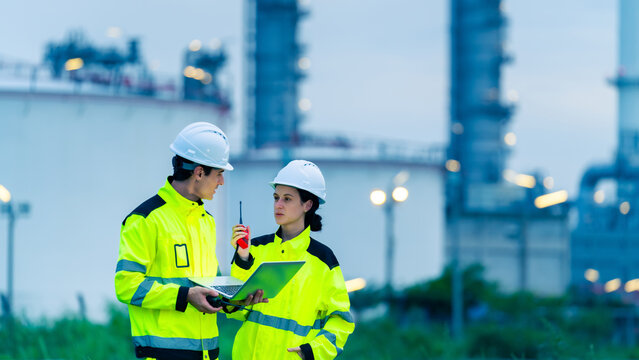 Petroleum refinery engineers and industrial workers working on laptop computer, inspection oil refinery plant at construction site at night, technician teamwork maintaining energy power system