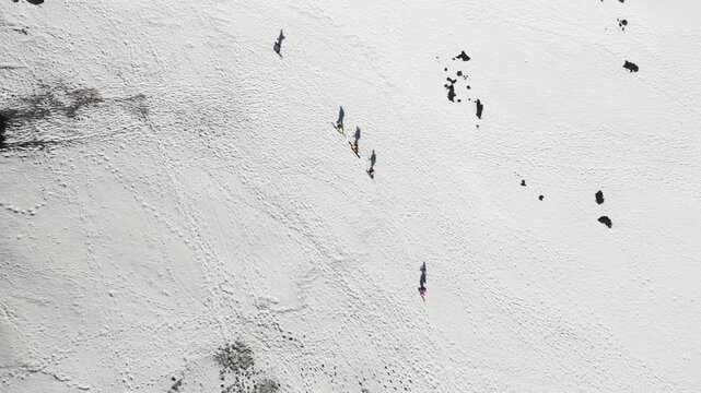 Aerial view of people walking on the snow-covered slopes near Rifugio Sapienza with volcanic rocks and long shadows in Nicolosi, Sicilia, Italy.