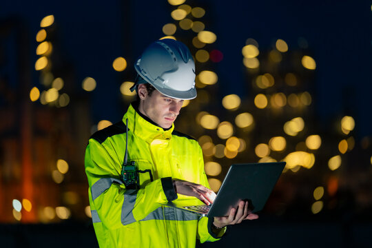 Male petroleum refinery engineers and industrial worker working on laptop computer, inspection oil refinery plant at construction site at night, technician maintaining energy power gas system