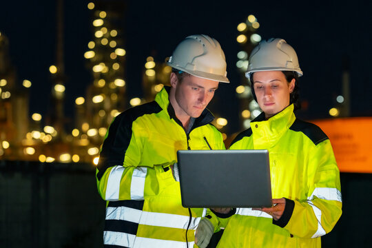 Petroleum refinery engineers and industrial workers working on laptop computer, inspection oil refinery plant at construction site at night, technician teamwork maintaining energy power system