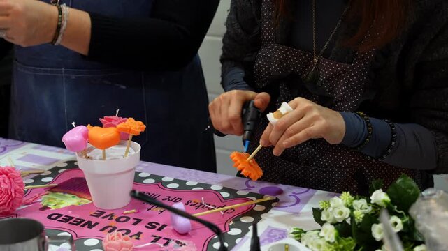 Female artisan using a blowtorch to craft a decorative wax flower during a candlemaking class