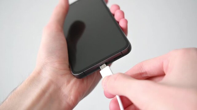 Hands plugging white usb c cable into smartphone showing battery charging screen