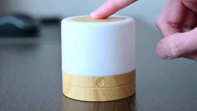 Hand touching the top of a glowing cylindrical wooden touch lamp on a dark table