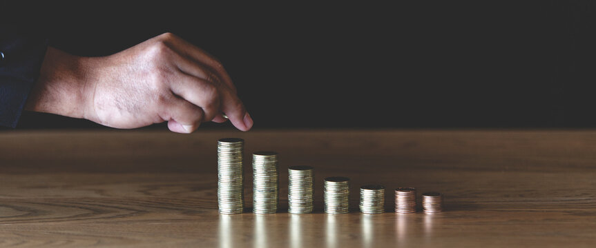 Hand pointing at stacks of coins on wooden table with dark background, symbolizing financial planning, savings, investment growth, business strategy, and money management concepts