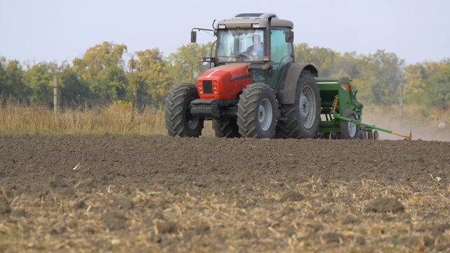 Agricultural tractor with seed drill plowing field during corn sowing, modern farming machinery cultivating soil and preparing farmland for crop planting in rural countryside