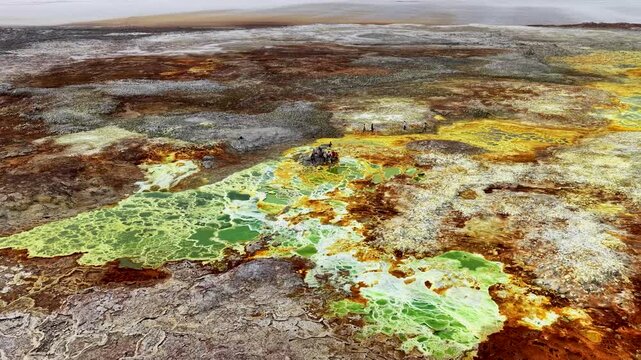 Aerial view of Danakil Desert hydrothermal pools with vibrant yellow salt formations and people standing on the volcanic landscape in Dalol, Afar, Ethiopia.