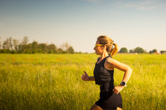 Athletic caucasian woman in black sportswear running on a country road on a sunny day. Background with copy space.