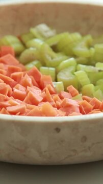 Vertical close-up of a glass bowl filled with freshly chopped carrots and celery prepared for cooking