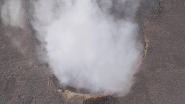 Aerial view of Erta Ale Volcano with thick white smoke rising from the crater and dark volcanic rock in Danakil Desert, Afar, Ethiopia.