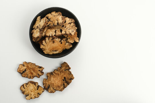 Dried ligusticum chuanxiong slices in a black bowl on white background top view