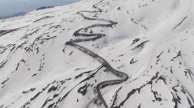 Aerial view of the winding road near Rifugio Sapienza on the snow-covered slopes of Mount Etna with hairpin turns and volcanic terrain in Nicolosi, Sicilia, Italy.