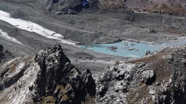 Aerial flyover over the mountain peaks next to Glacier de Cheilon with a pan up view from glacial lake to the mountain peaks of the Swiss Alps