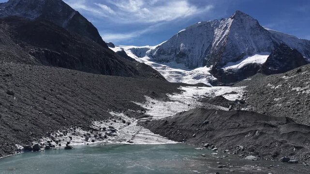 Aerial flyover over the iceberg filled glacial lakeof Glacier de Cheilon with a pan down view from the mountain peaks down to the ice and turquoise filled surrounding the icebergs and moraines
