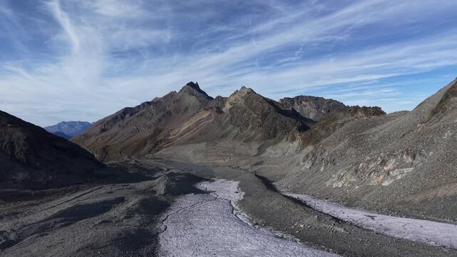 Aerial flyover over the glacial tongue of Glacier de Cheilon on a sunny summer day in the Swiss Alps with a pan down view towards the icy blue glacial lake.