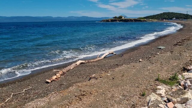 Secluded Agios Nikolaos Beach at the southern end of the Kassandra Peninsula in Chalkidiki, Greece, where gentle waves wash onto an untouched shoreline beneath a clear blue sky, completely empty
