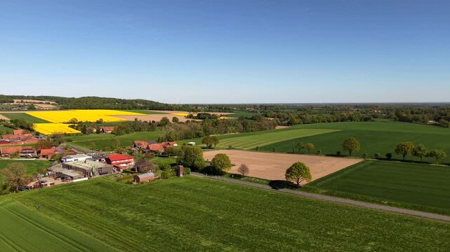 Rolling farmland landscape in Germany, Europe, with farmstead, cultivated fields, rural roads under clear blue sky and warm sunlight, showing peaceful countryside and agricultural scenery. Aerial wide