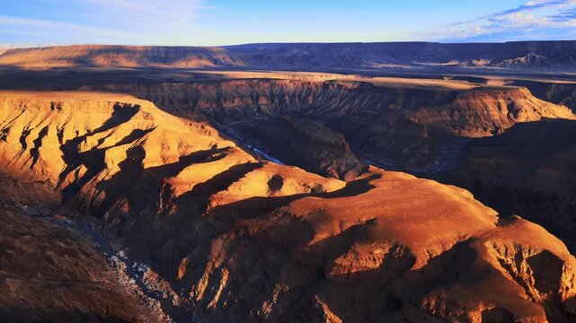 A drone flies over the rugged cliffs and rocky landscapes of Namibia, revealing vast open spaces bathed in warm sunlight, where dramatic textures and natural beauty meet in wild, cinematic harmony.