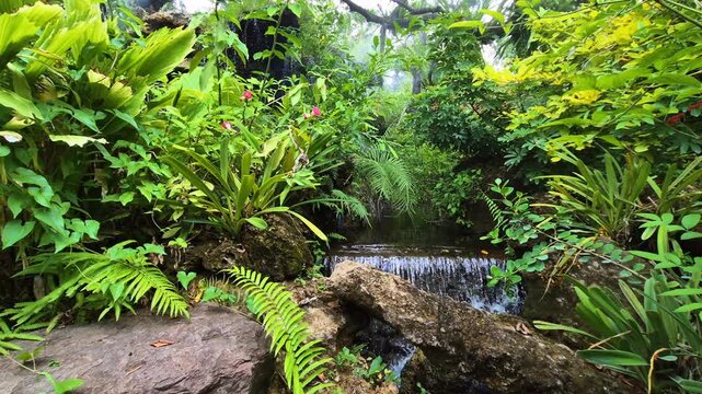 A waterfall in a garden surrounded by lush trees and vegetation, creating a relaxing atmosphere.