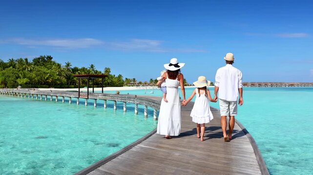A beautiful family in white summer clothing enjoys the view of a tropical island beach in the Maldives islands with turquoise ocean and palm trees