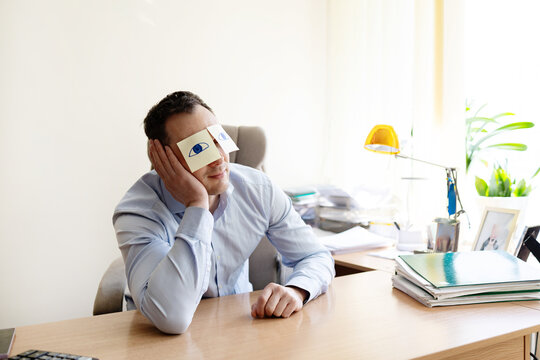 Man, sticky notes and sleeping in office, exhausted and professional with bad mental health. Male person, employee burnout and nap to recharge in workplace, eyes drawing and pretend awake at desk