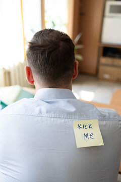Office prank with kick me message on sticky note. Funny day. April fish. Practical jokes. Inscriptions on the back. Stickers with jokes. Rear view of businessman with sticky note on his back in office