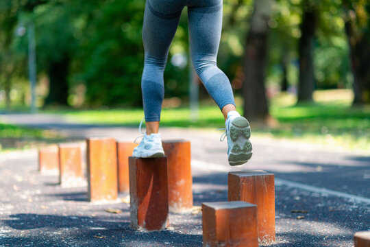 Close-up rear view of athletic woman stepping across wooden blocks, performing balance and coordination exercise outdoors.