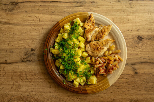 Top view of healthy lunch food. Green salad, chicken breast on grill, boiled potatoes and beans. Wood background. Home cooked meal