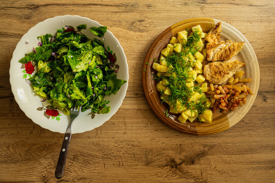 Top view of healthy launch food. Green salad, chicken breast on grill, boiled potatoes and beans. Wood background. Home cooked meal